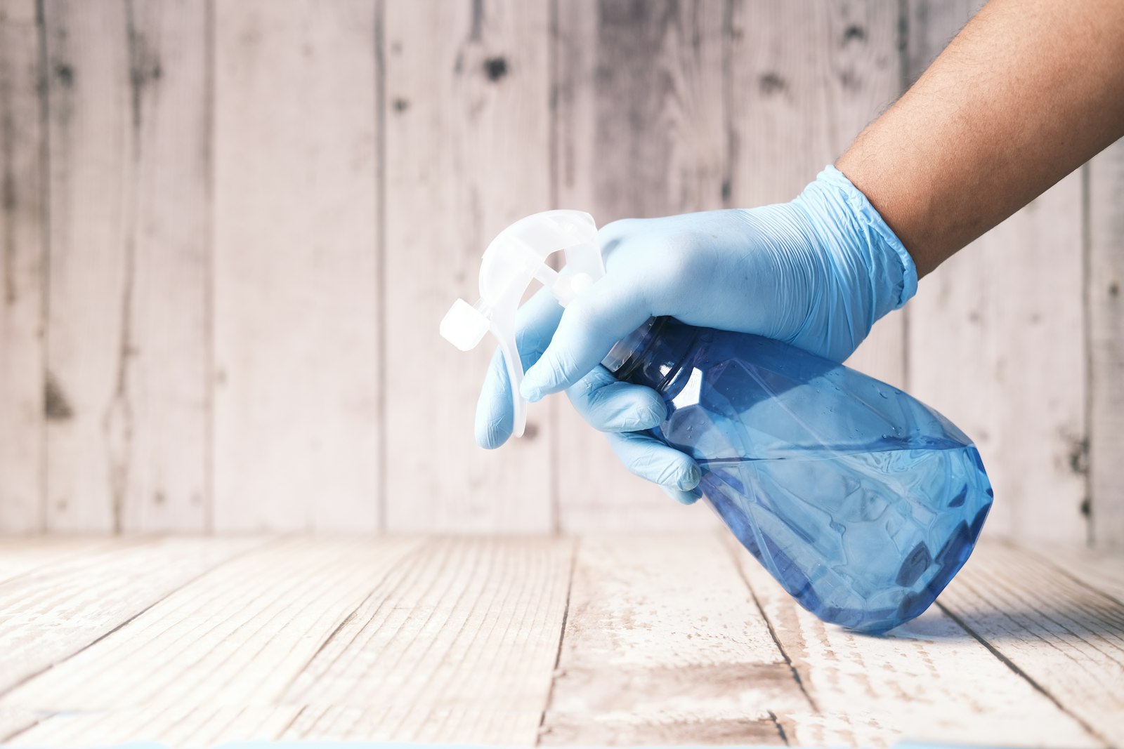 Gloved hand applying treatment spray from a blue bottle for a chemical washdown